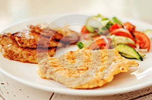 Chicken chop, vegetable salad and potato pancakes on a white plate