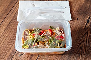 Chicken chow mein noodles in a plastic take away box or container on a wooden table. Quick and tasty Asian style meal for