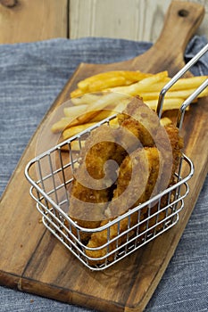 Chicken coujons coated in breadcrumbs in a wire metal basket, with fries