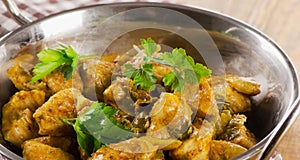 Chicken curry in a balti dish on wooden table.