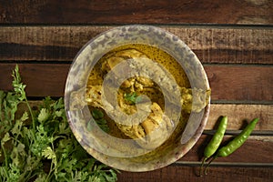 Chicken curry or masala , spicy reddish chicken leg piece dish garnished with coriander leaf and arranged in a white ceramic bowl