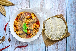 Chicken curry or masala , spicy reddish chicken leg piece dish garnished with coriander leaf and arranged in a white ceramic bowl