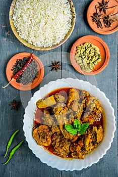 Chicken curry or masala , spicy reddish chicken leg piece dish garnished with coriander leaf and arranged in a white ceramic bowl