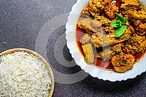 Chicken curry or masala , spicy reddish chicken leg piece dish garnished with coriander leaf and arranged in a white ceramic bowl