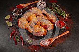 Kuřecí paličky marinované v talířích na černém pozadí s vařečkami a kořením, česnek, feferonka, rozmarýn