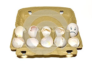 Chicken egg in a cardboard with painted emotions on shell among broken empty eggs in a paperboard. Broken eggs and eggs with a