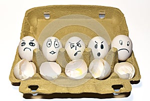 Chicken egg in a cardboard with painted emotions on shell among broken empty eggs in a paperboard. Broken eggs and eggs with a