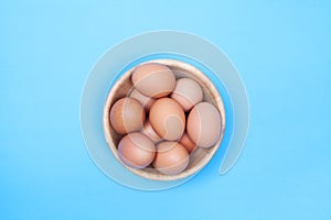 Chicken egg in wood bowl on blue background with space