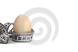 A chicken egg wrapped in a centimeter tape stands on a white background.