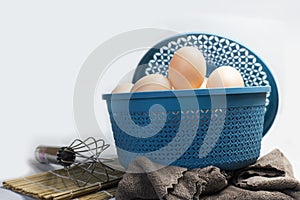 Chicken eggs in a blue plastic basket with a clean white back next to the basket The egg beater is ready for cook eggs