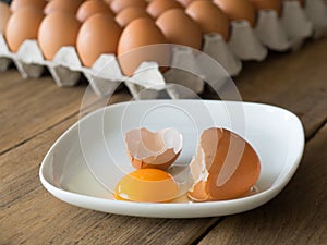 Chicken eggs cracked in white dish. The dish is placed on a wooden table.