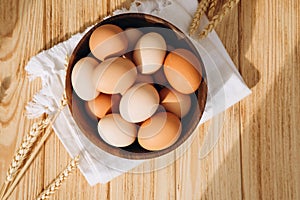 Chicken eggs of different brown and beige shades in a large wooden bowl on a wooden background with white kitchen towel