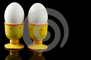 Chicken eggs in dotted eggcups on black