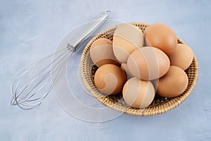 The chicken eggs with egg whisk on blue wooden background