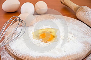 Chicken eggs, flour, whisk and rocking chair on the table. The process of making dough. Close-up. Broken egg in flour on a wooden