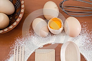 Chicken eggs, flour, wooden spoon and fork on the table. The process of making dough. Close-up. Broken egg.