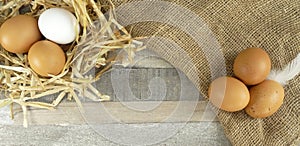 Chicken eggs in nest with burlap over wooden background