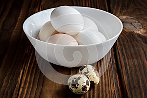 Chicken eggs in a plate and quail eggs on a wooden background
