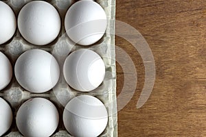 Chicken eggs are raw in the tray. The shell is white in eggs. In one section is an egg shell. On one egg lies a feather