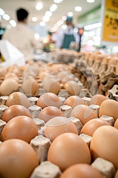 Chicken eggs on trays for sale in a supermarket with buyer and staff on the background