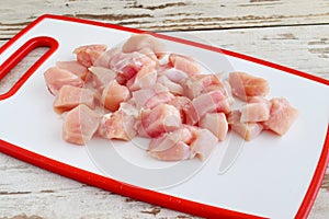 Chicken fillet cut in cubes on a white cutting board. Step by step cooking.