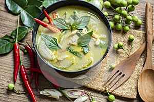 Chicken green curry Thai food on soup bowl with ingredient vegetable herbs and spices pepper chili on wooden table background,