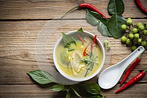 Chicken green curry Thai food on soup bowl with ingredient vegetable herbs and spices pepper chili on wooden table background,