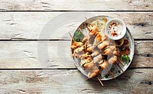 Chicken kebabs on skewers and savory cream sauce on grunge plate on natural wooden table