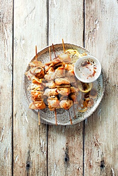 Chicken kebabs on skewers and savory cream sauce on grunge plate on natural wooden table