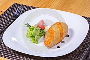 Chicken kiev with leaf salad and tomato on white plate