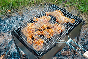 Chicken legs and wings are fried on coals in a brazier in a barbecue grill, marinated chicken is fried on a picnic