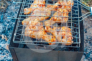 Chicken legs and wings are fried on coals in a brazier in a barbecue grill, marinated chicken is fried on a picnic