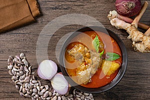 Chicken massaman curry in black bowl with herb and spices on wooden background.