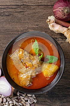 Chicken massaman curry in black bowl with herb and spices on wooden background. Thai authentic food called massaman kai.