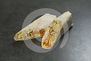 Chicken meat shawarma isolated on dark stone background. Gyros wrapped in lavash bread