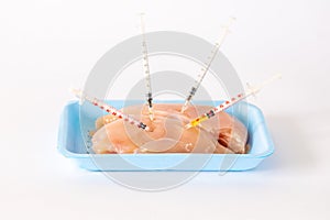 Chicken meat on a tray with syringes stuck in it, Nutrition concept, antibiotics in meat, Chemically stuffed food, White