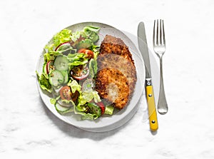 Chicken milanese and fresh romaine salad, cherry tomatoes, radishes, cucumbers salad - delicious lunch on a light background, top