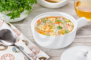 Chicken orzo soup in a white crock on wooden background. Italian soup with orzo pasta photo