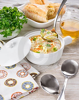 Chicken orzo soup in white crock on wooden background. Italian soup with orzo pasta. Ladle. Bread. Glass of wine.