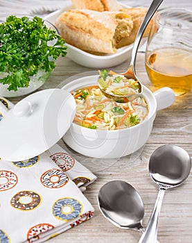 Chicken orzo soup in white crock on wooden background. Italian soup with orzo pasta. Ladle. Bread. Glass of wine. photo