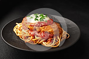 Chicken parmigiano with linguini pasta on a plate black background