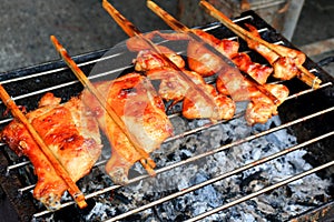 Chicken part grilling on grate above charcoal stove.