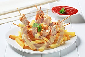 Chicken pieces on sticks and French fries