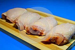 Chicken pieces on a wooden board on a blue background.