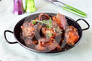 Chicken with prunes cooked in the oven in a black bowl on a textile background.