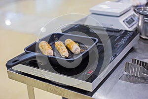 Chicken rolls or bangers frying in pan on electric stove at restaurant
