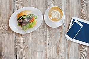 Delicious breakfast on the table. Chicken sandwich, Cup of coffee and smartphone on the table