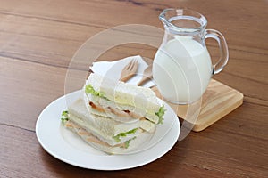 Chicken sandwiches on white dish with milk and wooden fork and spoon.