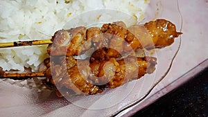 chicken satay and rice on a glass plate.