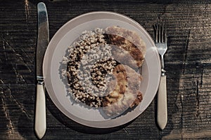 Chicken schnitzel with buckwheat on plate over wooden background. Top view, flat lay photo